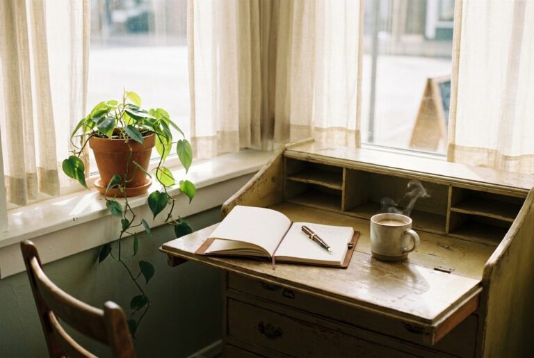 A cozy writing desk with a notebook, coffee, and a plant by a window